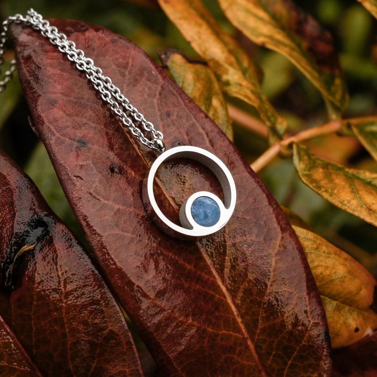 Collier "Pigment Collier" avec un design moderne en marbre et argent sur fond texturé.