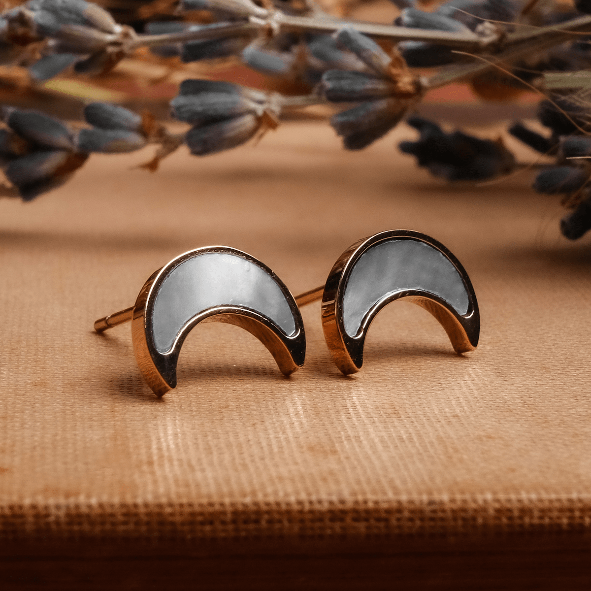 "Hue Earrings": Elegant crescent-shaped earrings in white nacre and rose gold, set against a rustic background.