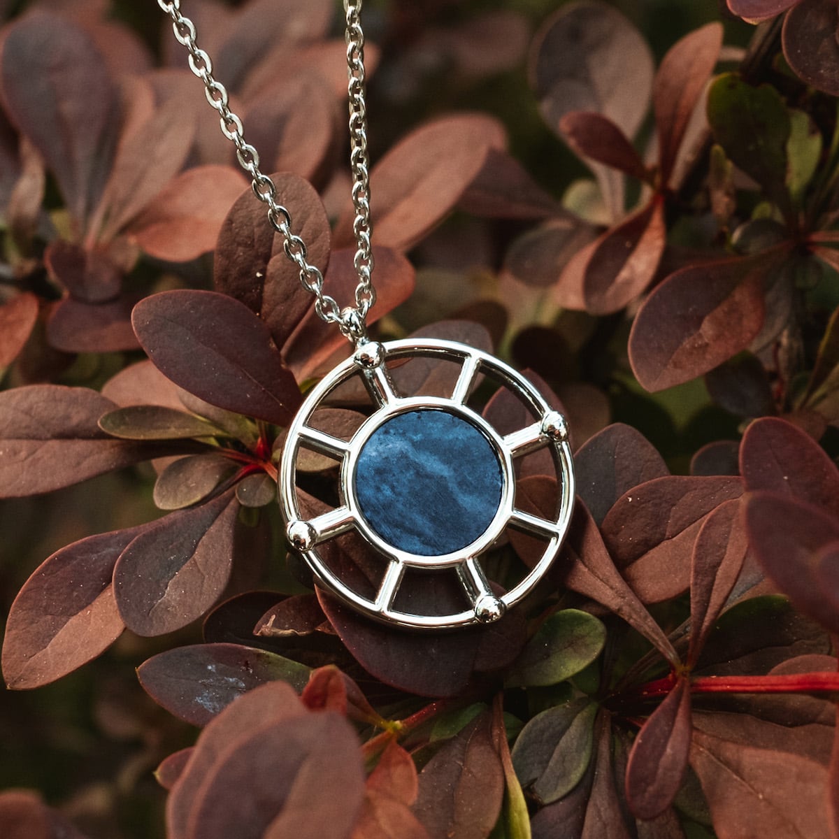 "Amulet Necklace" necklace with a silver frame and marble centerpiece, featuring an elegant and natural style against foliage.