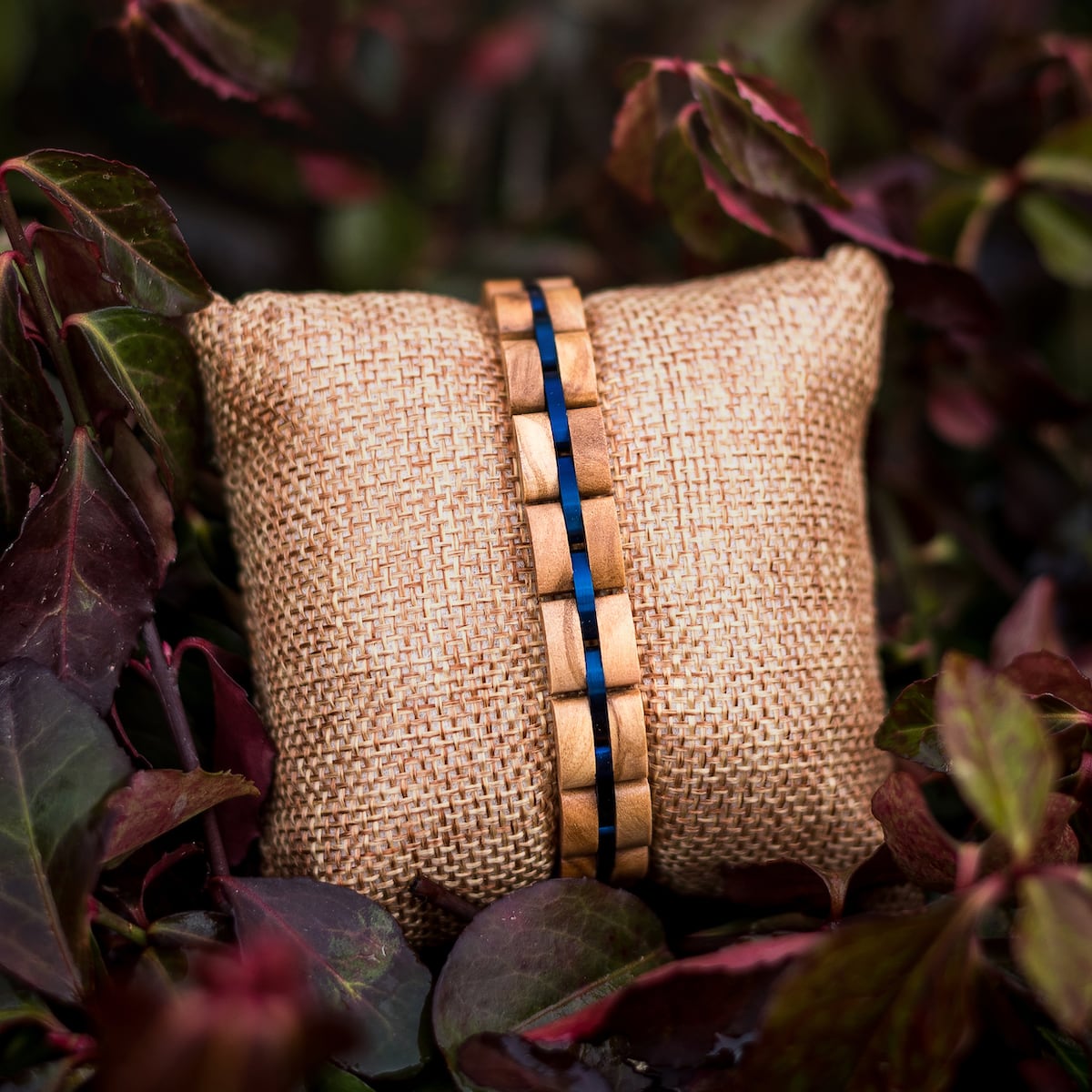 "Fantasia" armbånd udformet med olivewood og blå accenter, præsenteret på burlap midt blade.