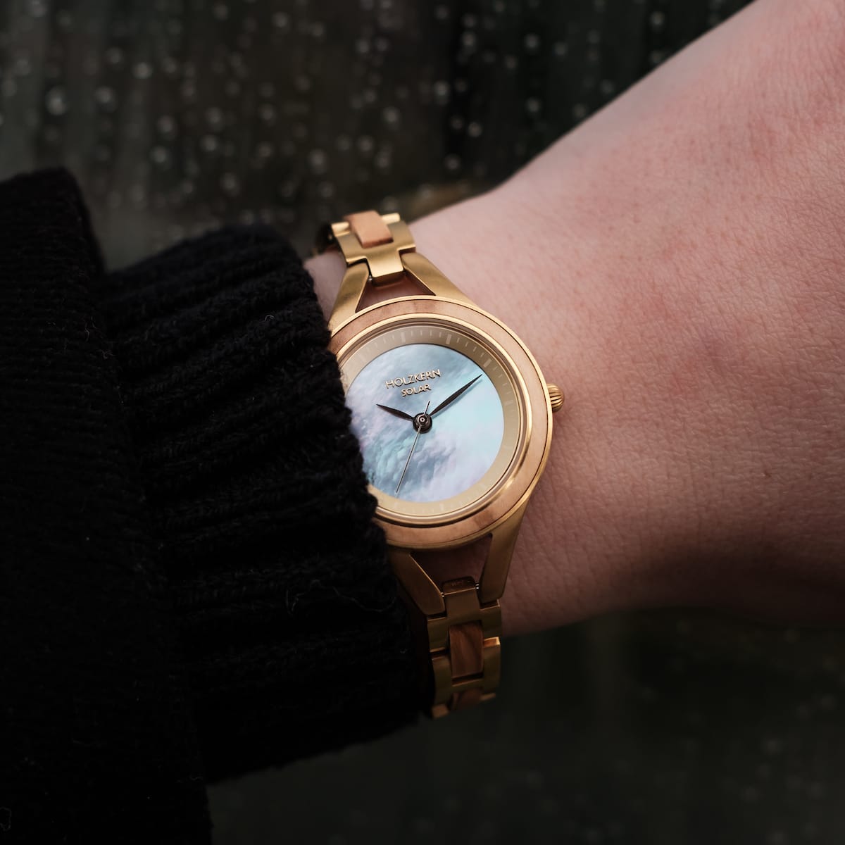 Orologio "Tumi" con accenti di ulivo e stile nacre sul polso, caratterizzato da un design visivo classico ed elegante.