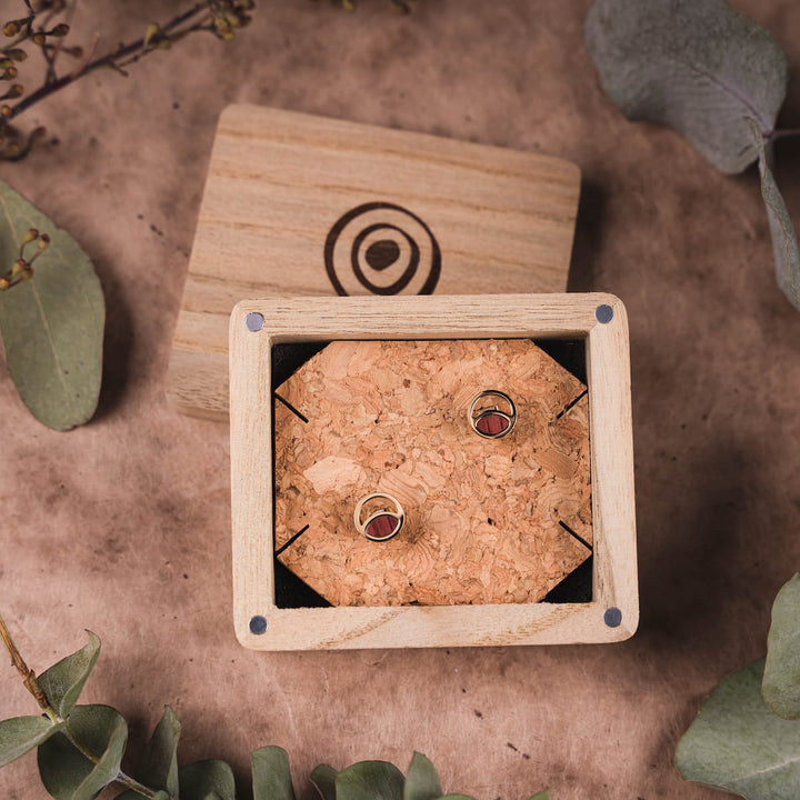 "Perception Earrings" earrings featuring amaranth and gold tones, presented in a wooden box with natural accents.