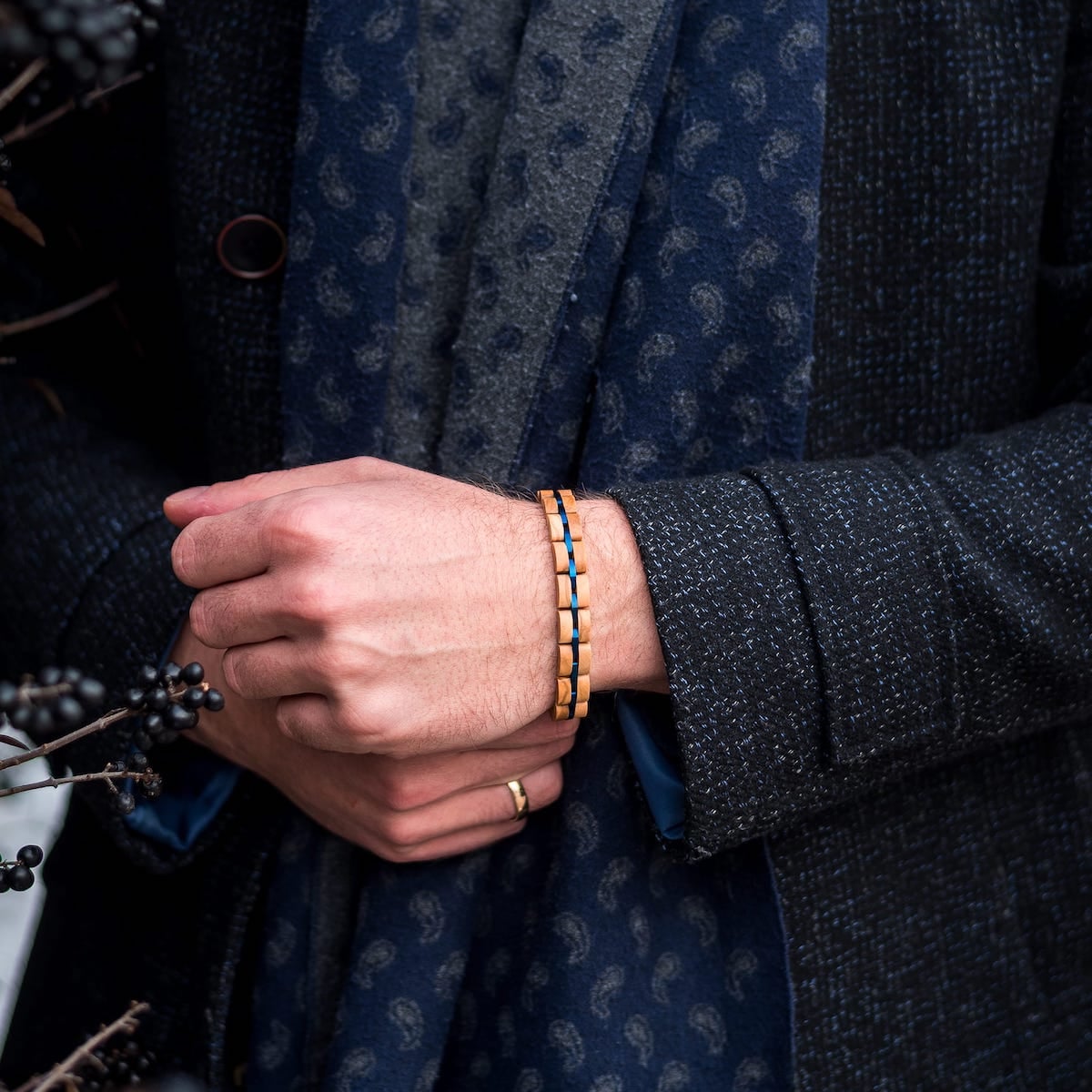 "Fantasia" armbånd med en stilfuld olivewood og blå design på et håndled mod en tekstureret mørk jakke baggrund.