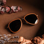 "The Honorable" sunglasses, featuring a teak frame and matte gold accents with a stylish, earthy aesthetic.