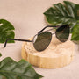 Occhiali da sole "The Badass II" caratterizzati da un design in legno di piombo e argento antico su un display in legno naturale con foglie tropicali.