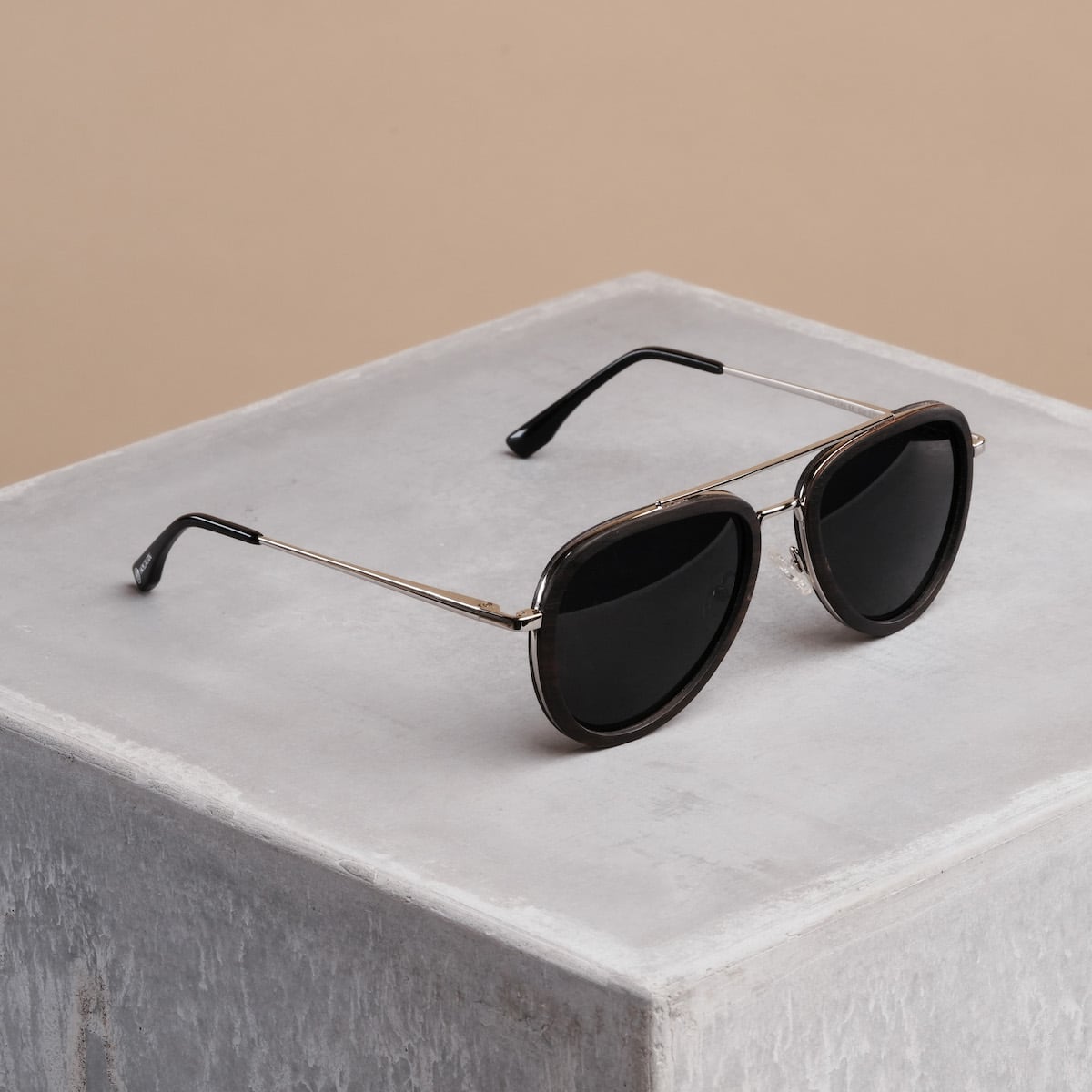 "The Honorable" sunglasses in a sleek leadwood and silver design on a minimalist concrete background.