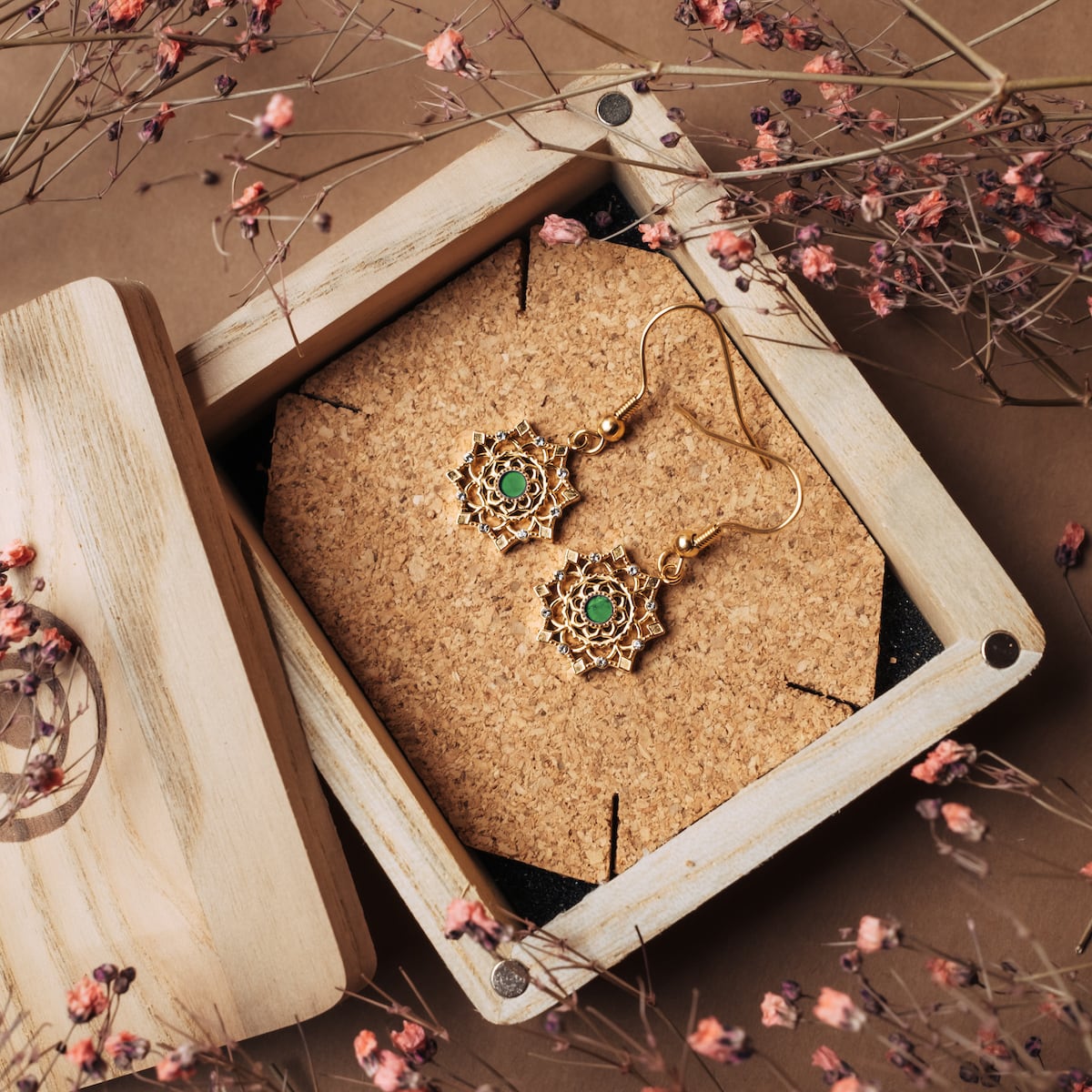 "Aphonia Earrings", jade and gold earrings with intricate floral design, displayed in a wooden box surrounded by delicate dried flowers.