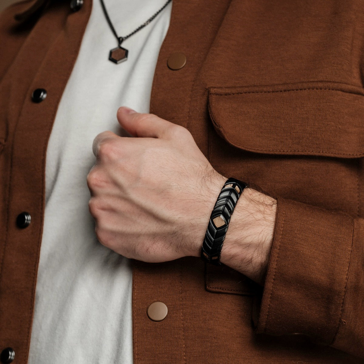 "Prelude" bracelet, featuring a sleek black and koa wood design, worn with a casual brown jacket and white shirt.
