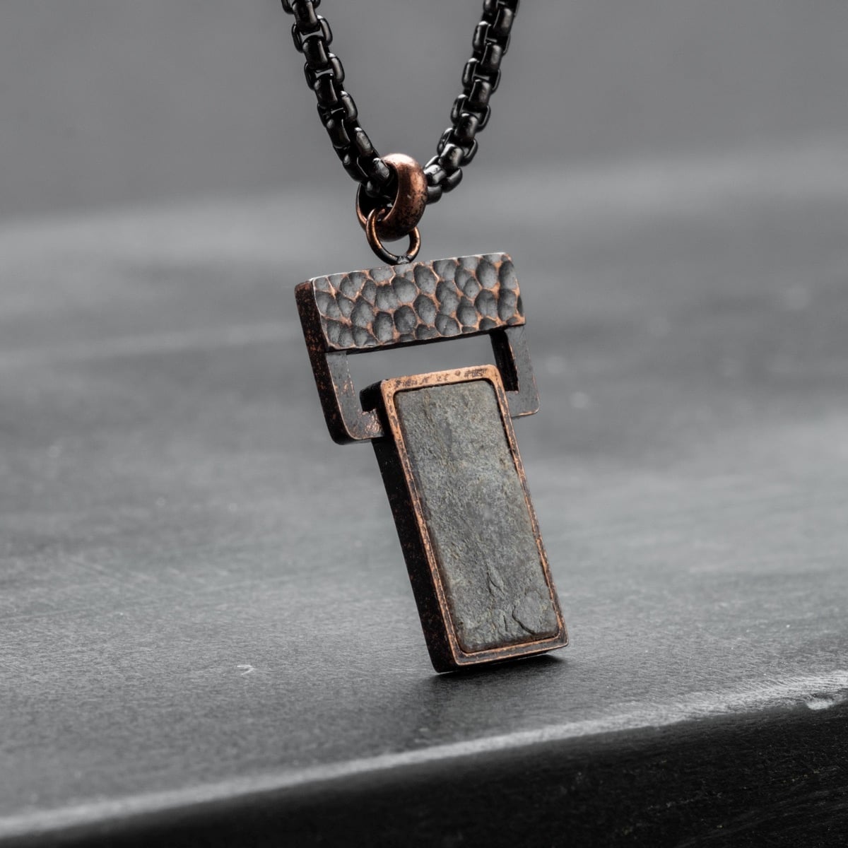 "Transcendent" pendant with slate and antique bronze finish, featuring a textured, modern design.