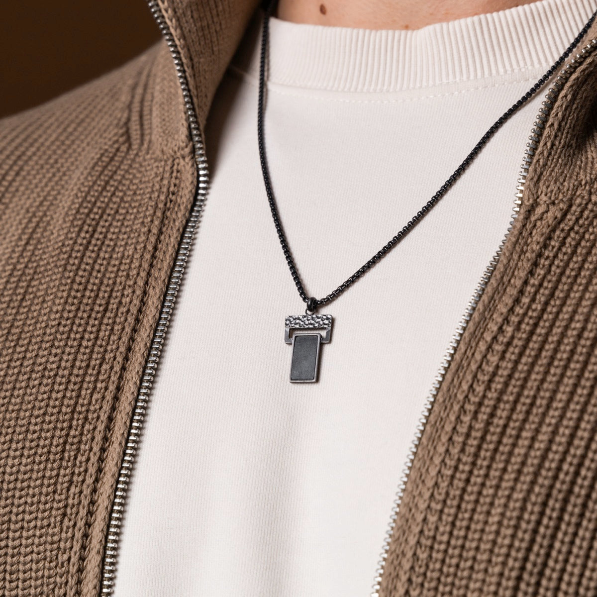 "Transcendent" necklace with slate and antique silver detailing, worn with a beige knit zipper jacket.