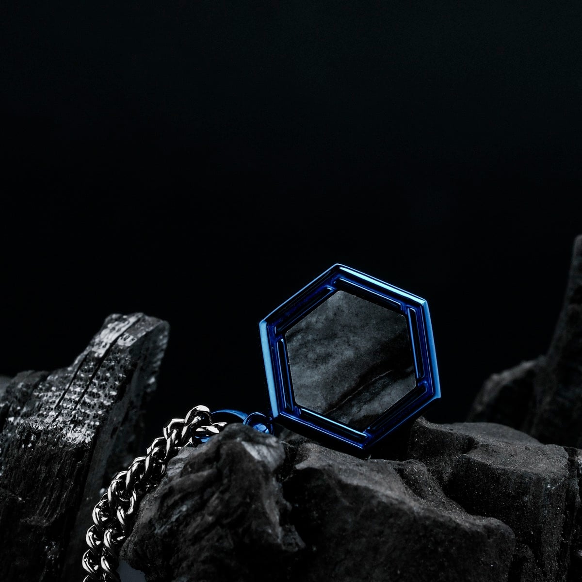 "Axis Necklace", a stylish necklace featuring a hexagonal blue frame with Picasso Jaspis stone, set against a dark background.