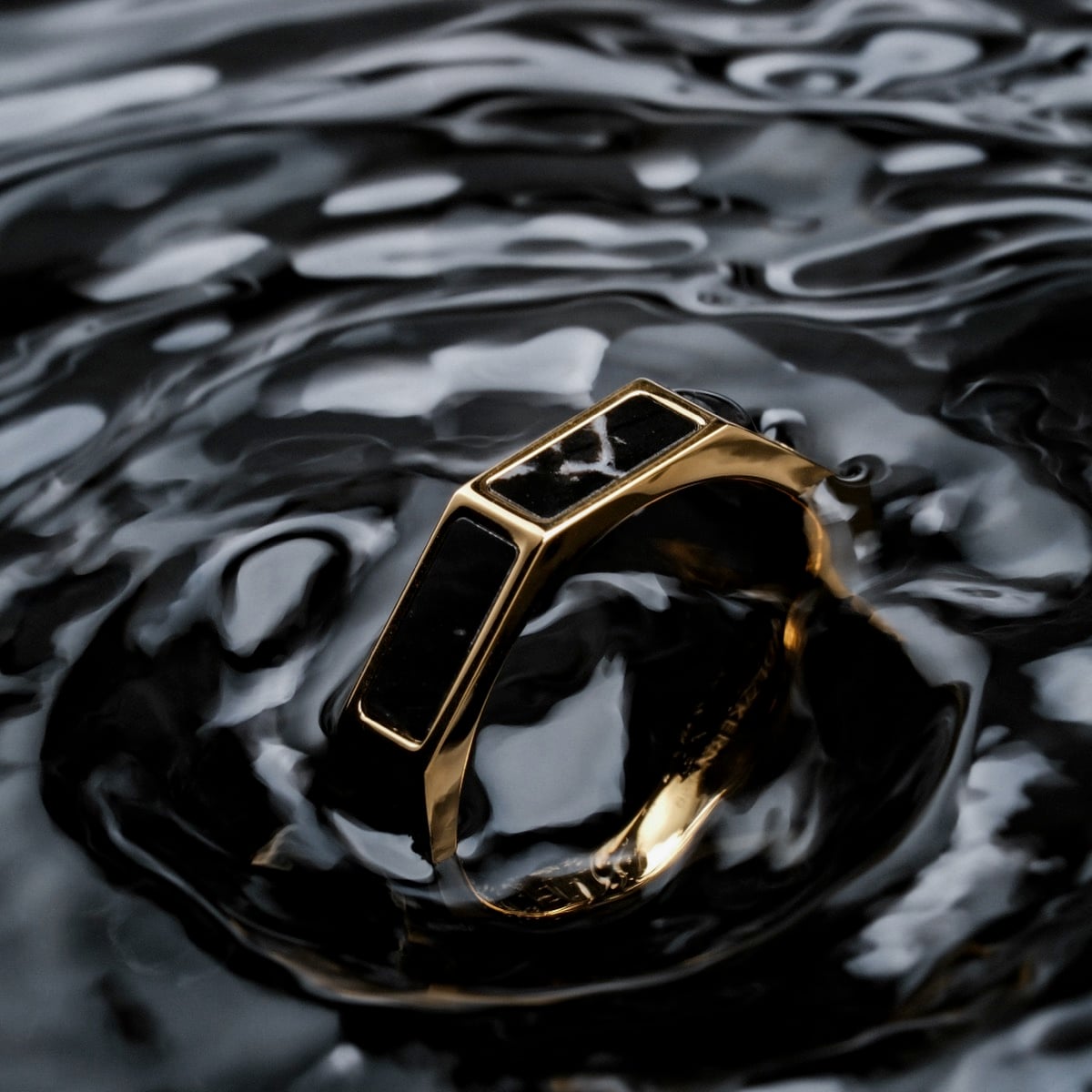 "Supremum Ring" ring, featuring a luxurious marble and gold design, elegantly showcased on a reflective surface.