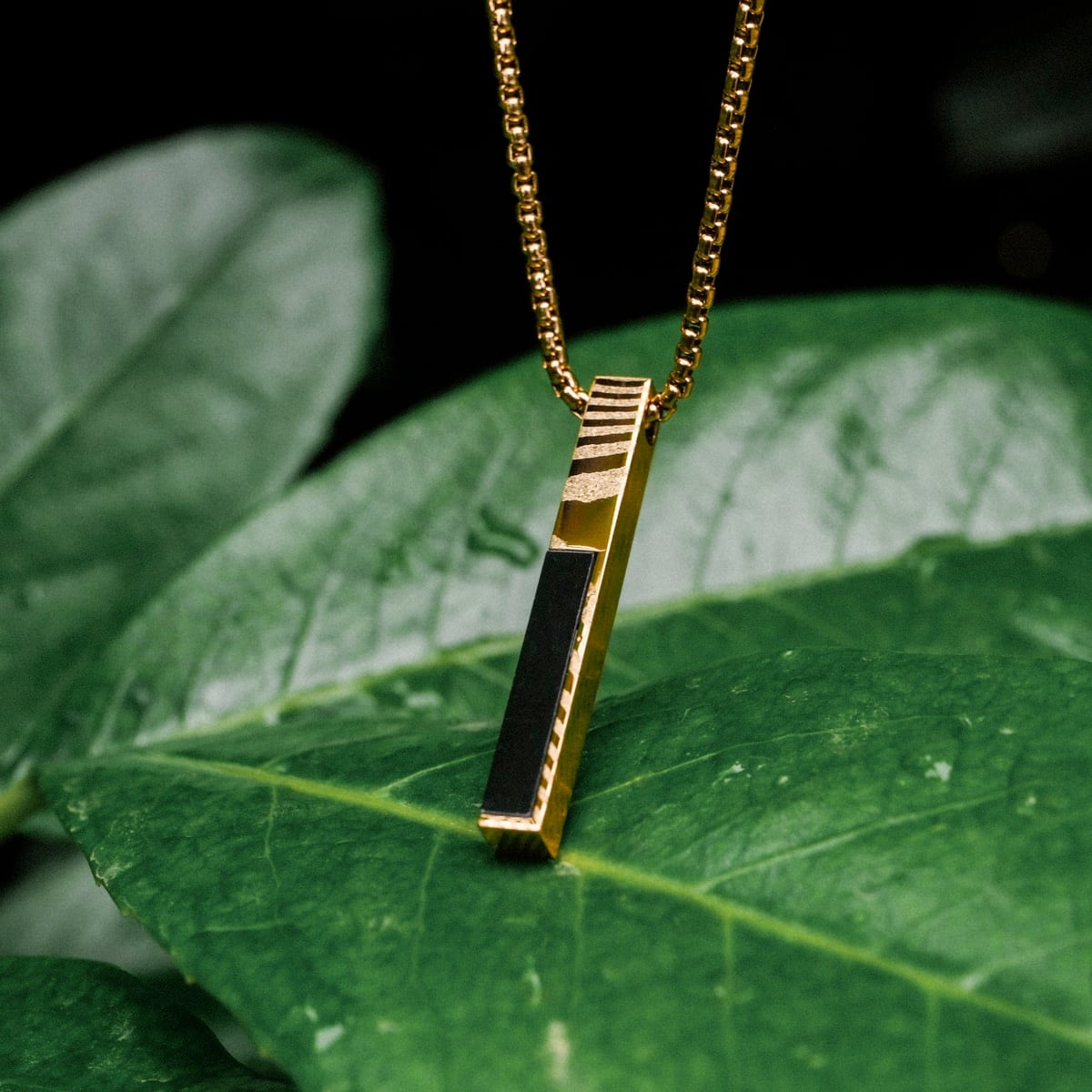 "Campania Necklace" necklace featuring a rectangular black marble and Damascus design, set against lush green foliage.