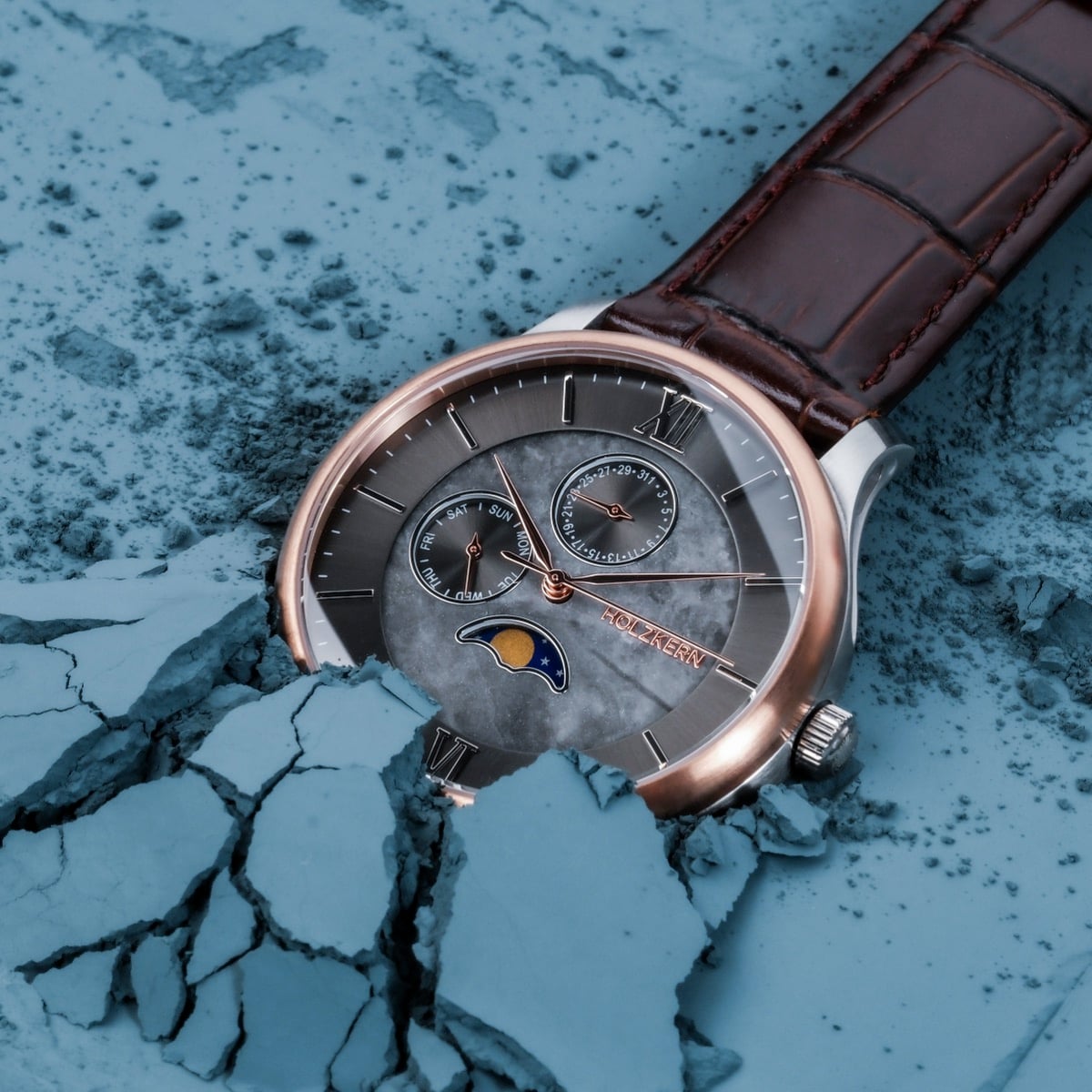 "Moonrise", a wristwatch with a marble dial and dark brown leather strap, set against a textured blue backdrop.