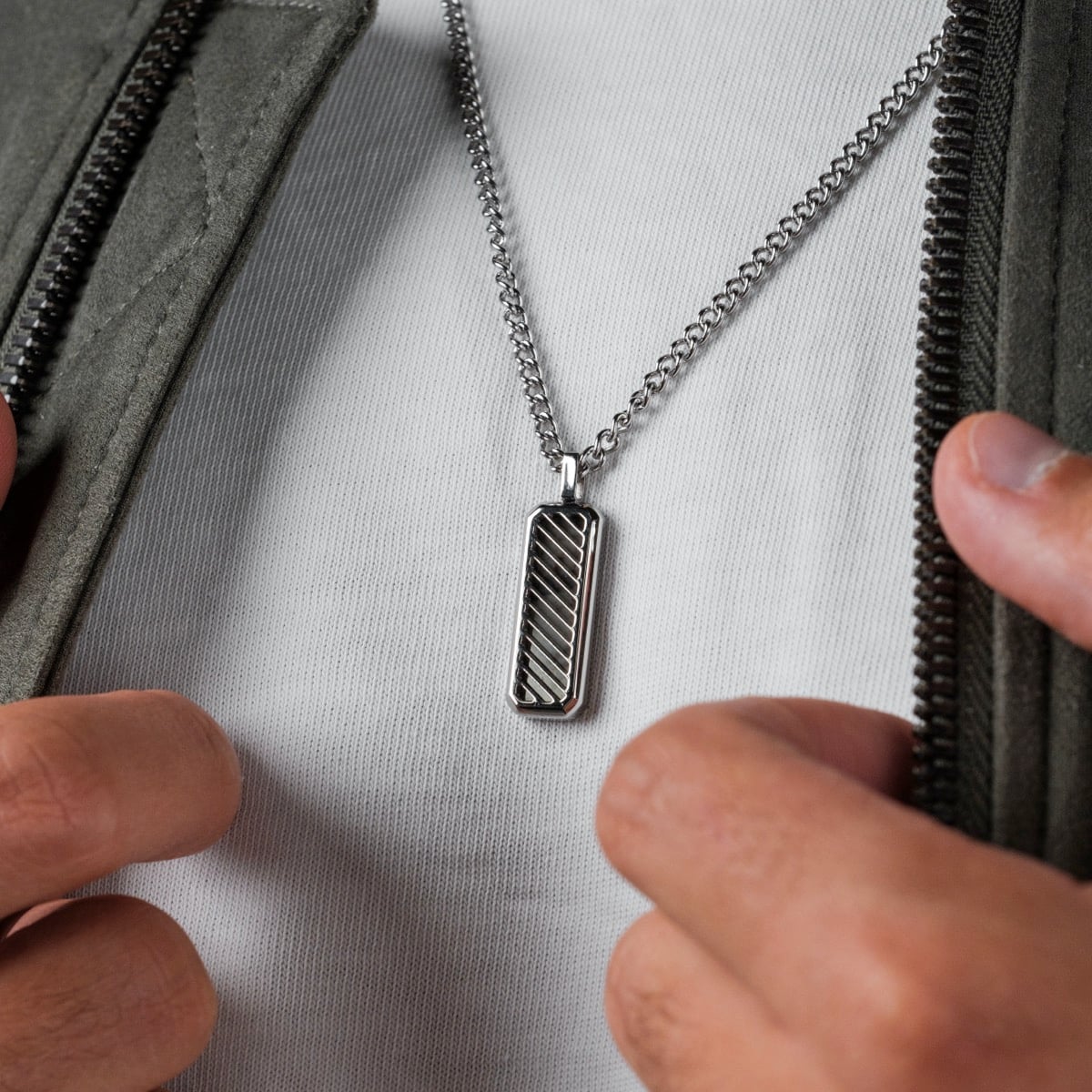 "Interplay Necklace" pendant necklace featuring a gray marble and silver design, worn against a white shirt with a jacket.