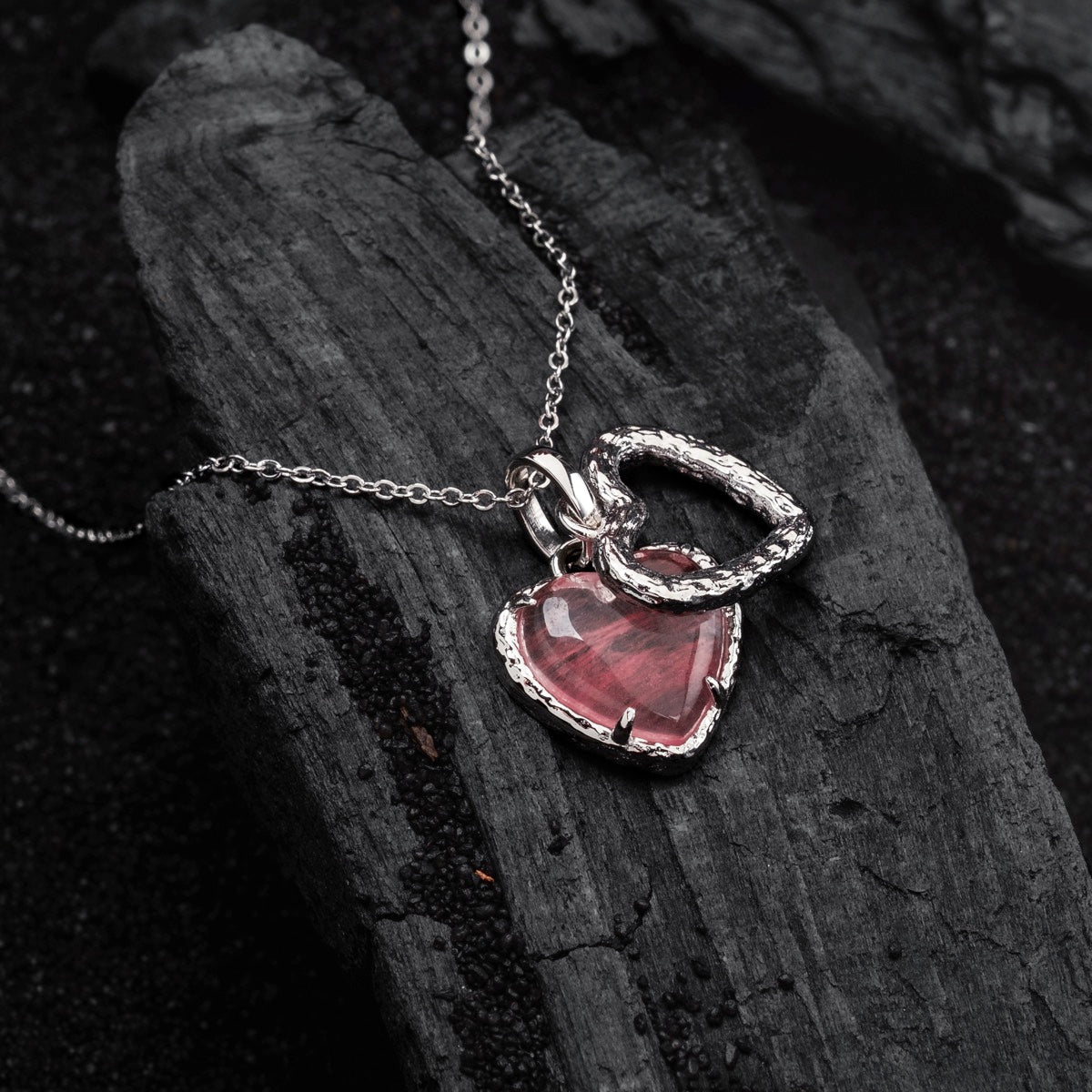 "Collana di ammonio", una collana di quarzo a forma di cuore e argento, elegantemente esposta su sfondo scuro texture.