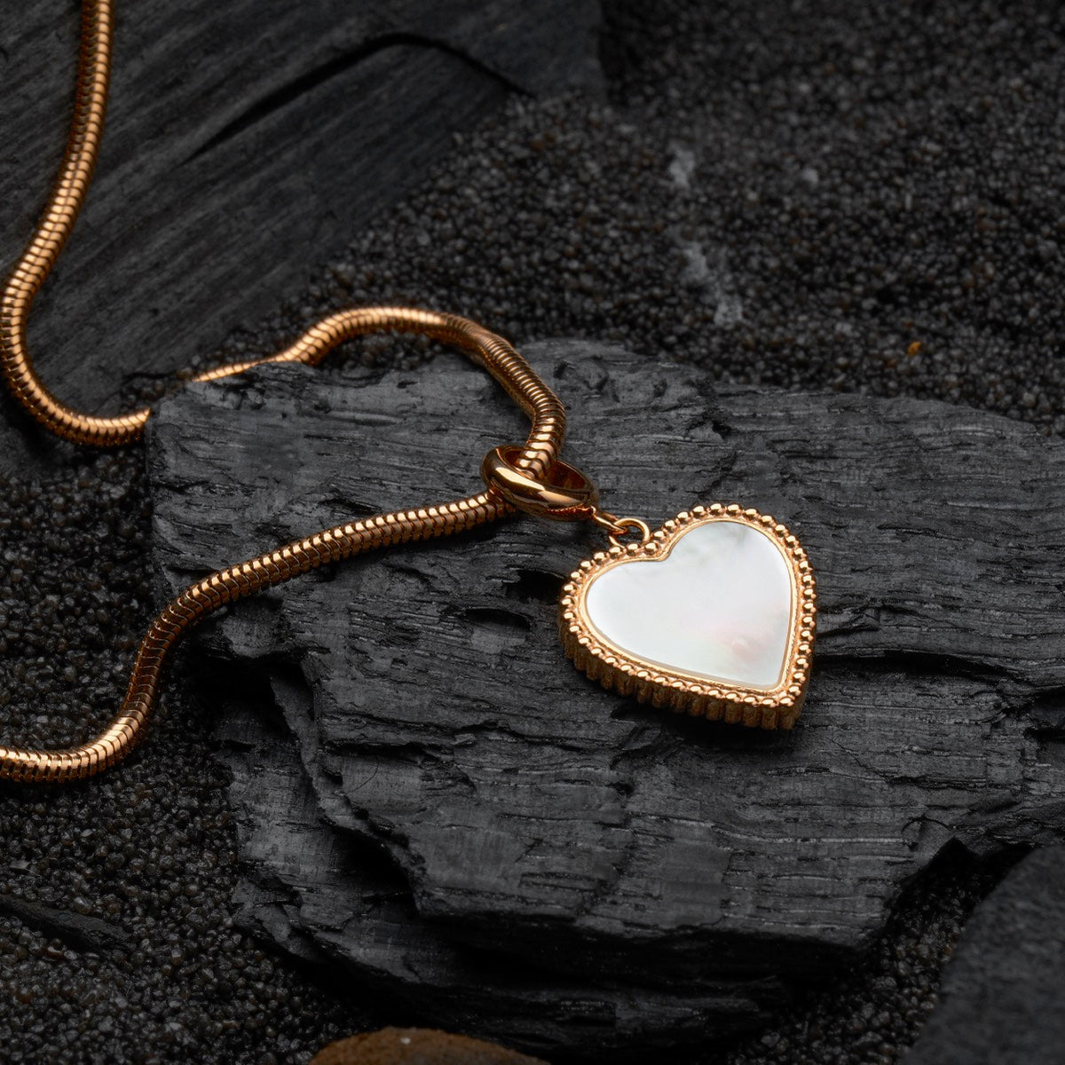 "Amorance Collier", un collier élégant avec un pendentif en nacre en forme de cœur et chaîne en or rose sur un fond texturé foncé.