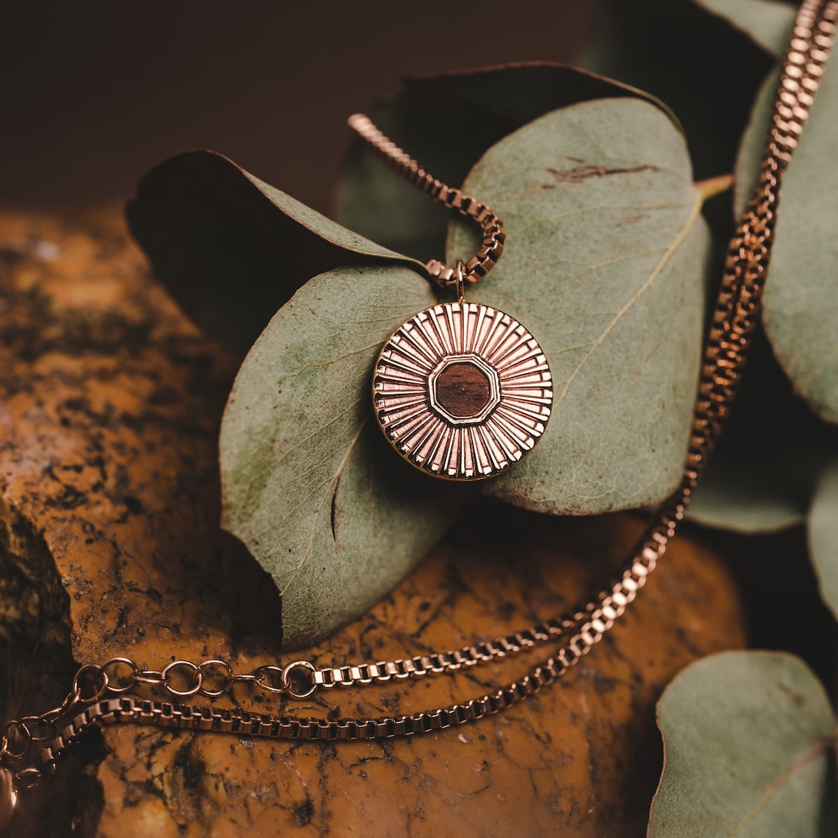 "Stencil Necklace": Elegant necklace with walnut center and rose gold accents, featuring a round, intricate pendant design.