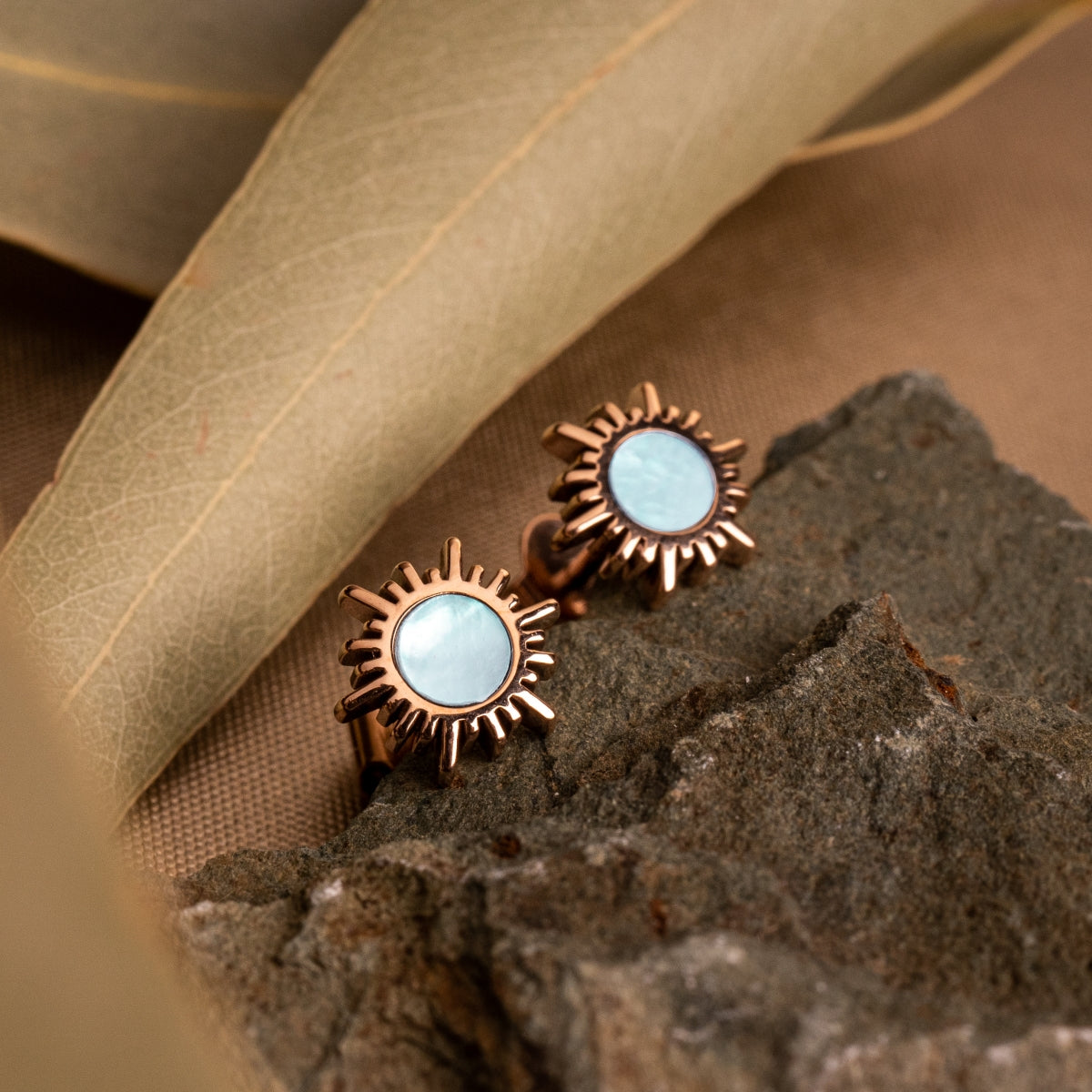 "Shade Earrings": Elegant earrings in rose gold with a sunburst design and blue nacre center.