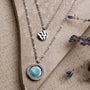 "Zendala Necklace" necklace in nacre and silver, featuring layered pendants on a textured background with dried lavender accents.
