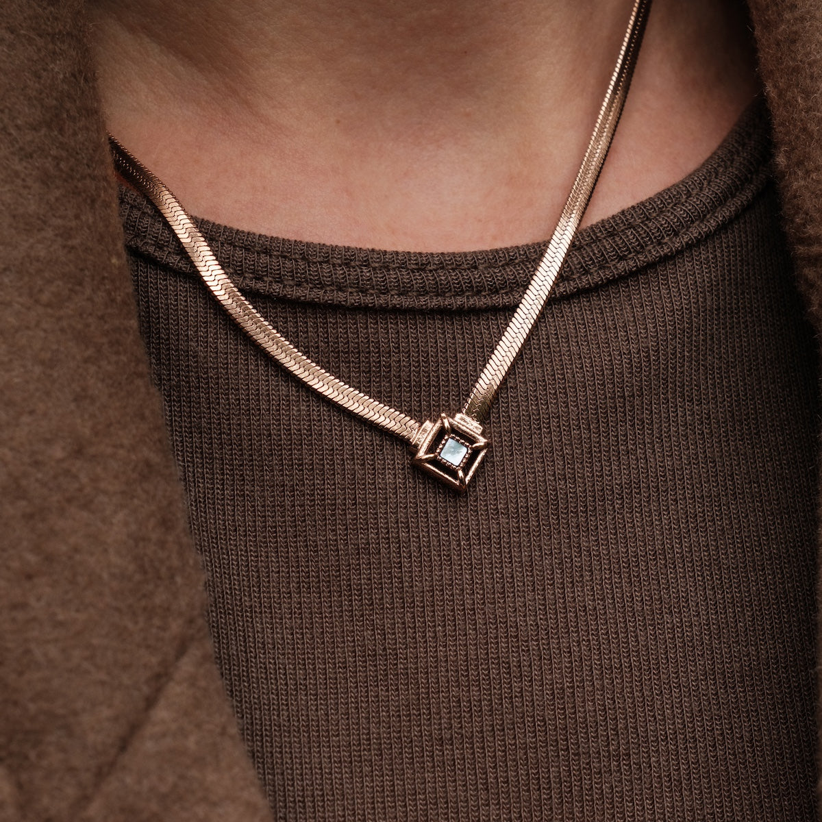 "Awakening Necklace" necklace, featuring a nacre and rose gold design, worn over a textured brown top.