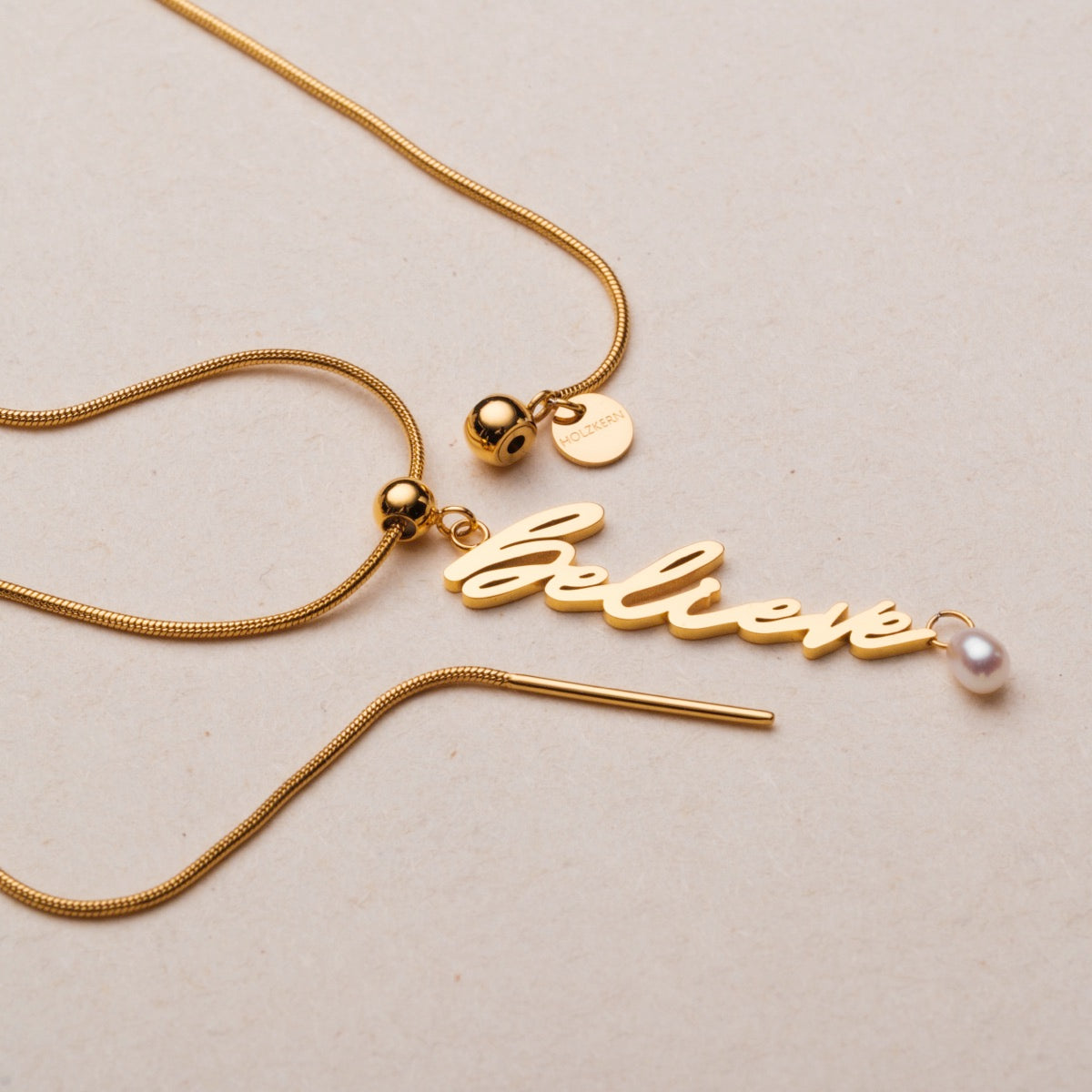 "Calma de creer" collar en oro con acento de perlas, con un diseño elegante de encanto de script.