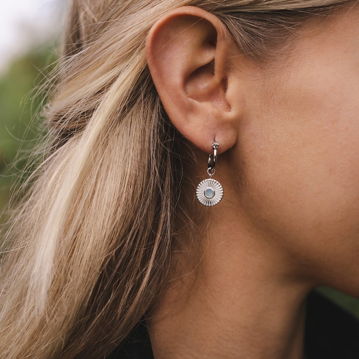 "Stencil Earrings", round aquamarine and silver earrings with a modern, elegant design worn by a person.