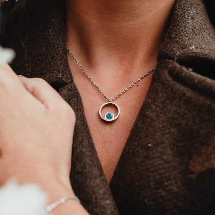 Collier "Pigment Collier", avec un design en marbre et argent, porté élégamment sur un fond de tissu texturé.