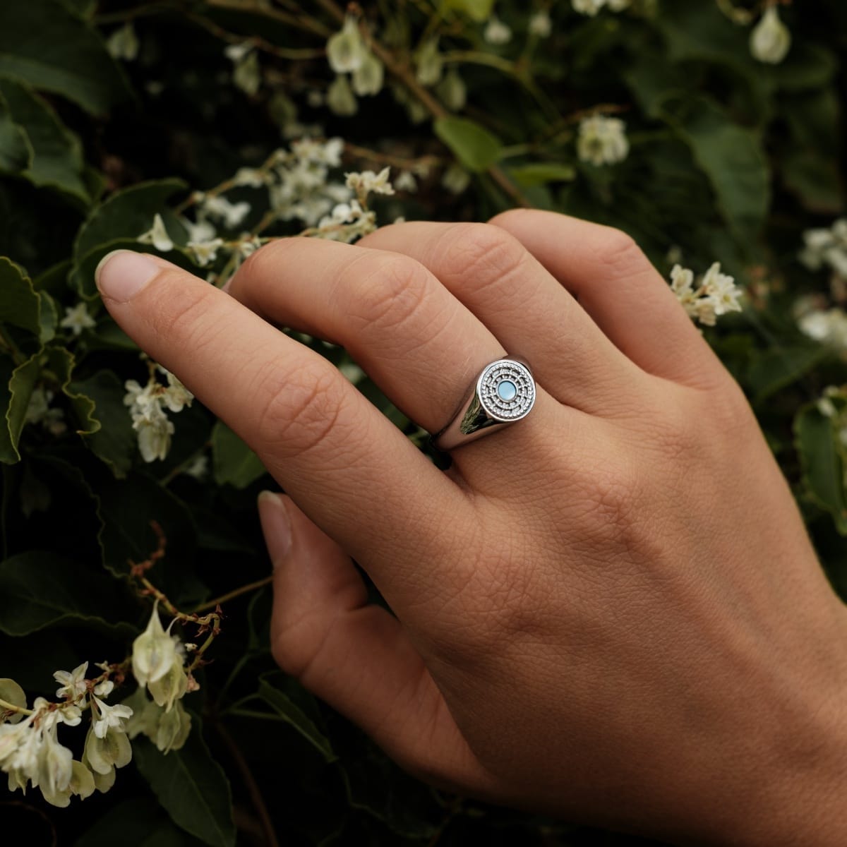 "Pixa Ring" ring features nacre and silver, showcasing an elegant, detailed design on a hand amidst natural foliage.