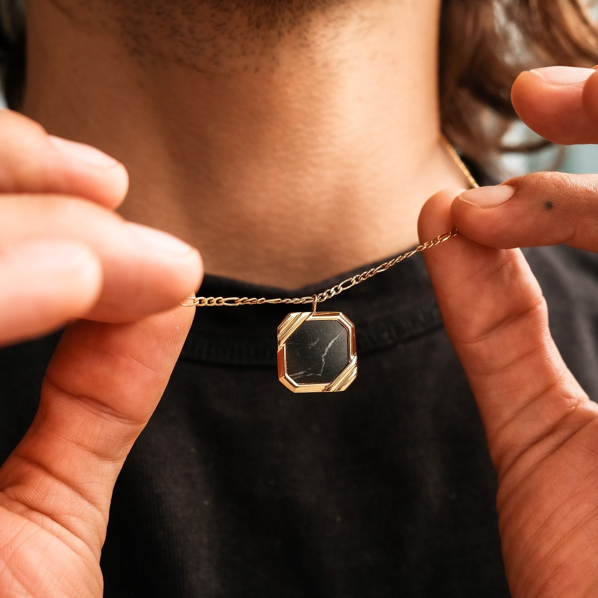 "Scalar Ketting" ketting met een marmer en goud ontwerp elegant held door een persoon.