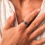 "Numerieke ring," een stijlvolle ring met Koa hout en zilver accenten, weergegeven op een hand dragend een structured wit weefsel.