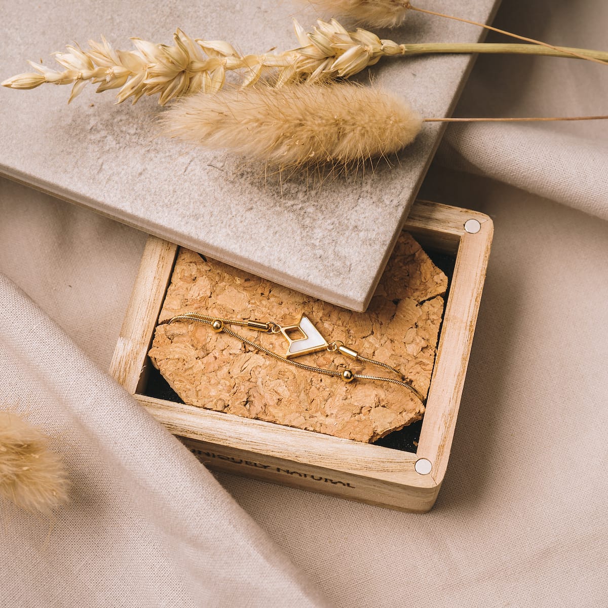 "Conceptual Bracelet", a stylish bracelet, featuring nacre and gold elements, presented on a natural cork and wood backdrop.