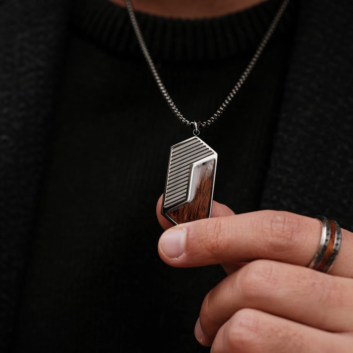 "Zigzag Necklace", a geometric walnut and dark grey necklace, held by hand for a sleek, modern look.