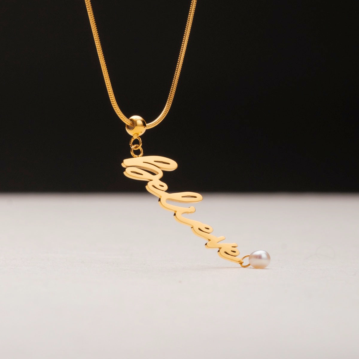 "Calma de Creencia", un collar de encanto dorado con un acento de perlas, elegantemente diseño cursivo.