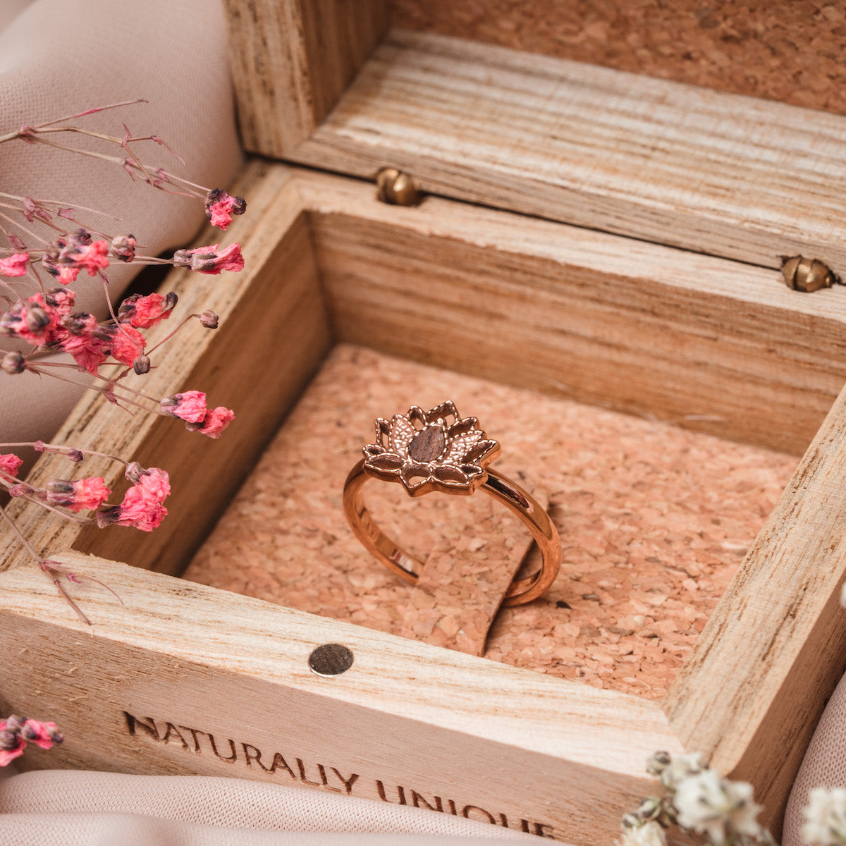 "Balance Ring", a walnut and rose gold ring, elegantly displayed in a rustic wooden box with floral accents.