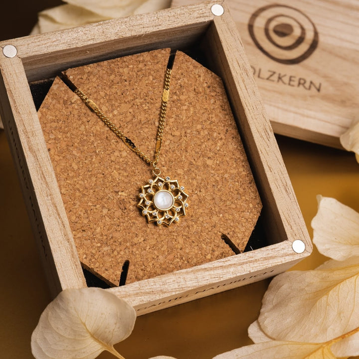 "Composition Gem Collier", un élégant collier en pierre de lune et en or au design complexe, exposé dans une boîte en bois.