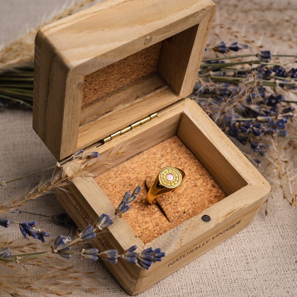 "Pixa Ring", a stylish gold ring with pink nacre, elegantly displayed in a wooden box with lavender accents.