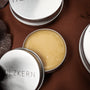 "Wood Care Balm 100ml" stagno, un elegante balsamo per la cura del legno con una texture liscia e un imballaggio in metallo lucido.