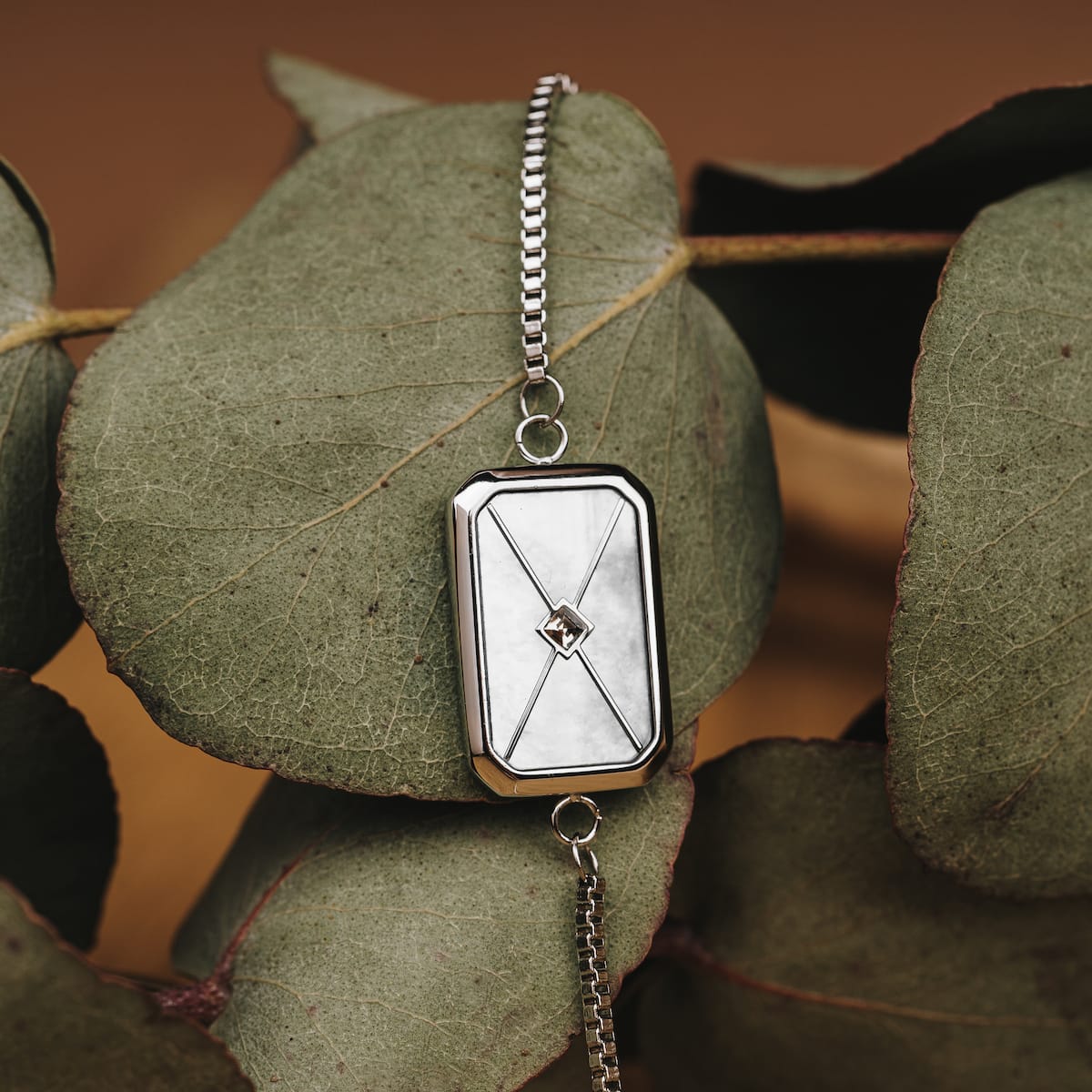 "Aquarell Bracelet", a sleek bracelet with white nacre and silver accents, displayed elegantly against a leaf background.