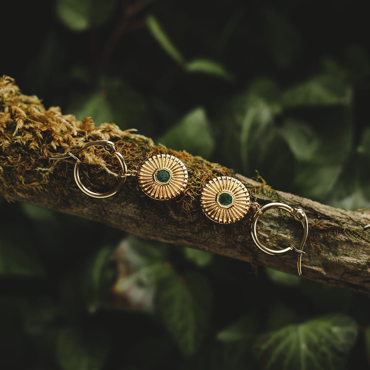 "Stencil Earrings": Elegant earrings with a marble and gold design, resting on a natural branch background.