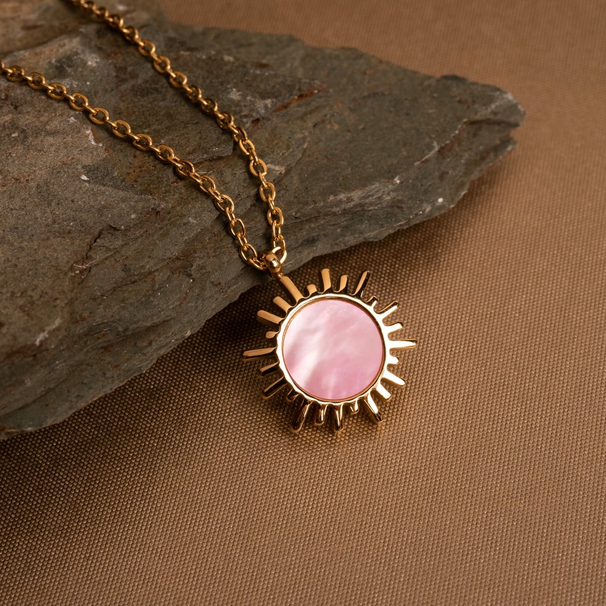 "Shade Necklace" necklace with a pink nacre sunburst pendant on a gold chain.