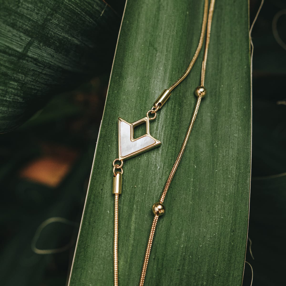 "Conceptual Bracelet" bracelet with nacre and gold materials, featuring a minimalist and elegant design on green foliage.