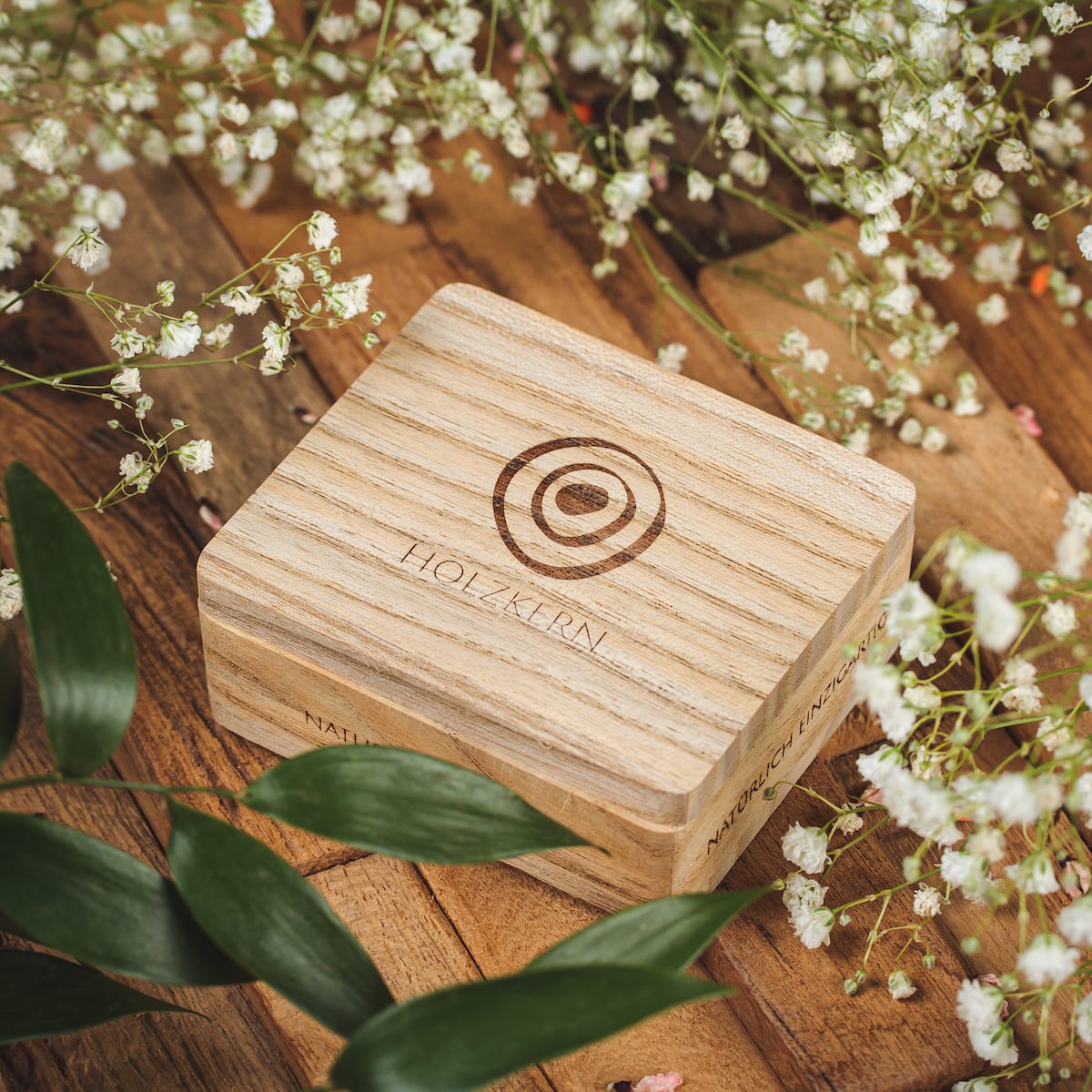"Biżuteria Single- Box" drewniane pudełko biżuterii z wygrawerowanym designem, otoczony delikatnymi kwiatami na rustykalnej drewnianej powierzchni.