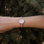 Montre "Alva" avec une face en marbre et des accents en or rose, avec un bracelet rose sur fond vert naturel.