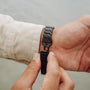 "Baritone" watch with marble and black design, featuring a sleek, modern style clasp being fastened on a wrist.