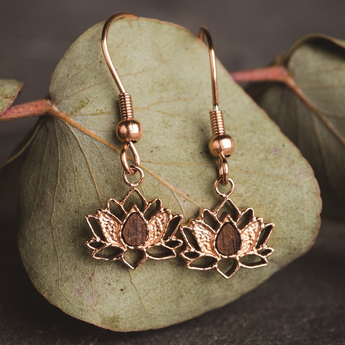 "Balance Earrings" earrings in walnut and rose gold, featuring a delicate floral design against a leafy backdrop.