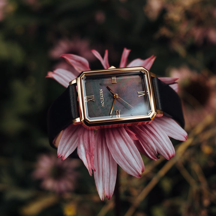 La montre "Auctoritas" est ornée d'un cadran nacre et d'accents dorés, élégamment exposés sur un fond floral doux.