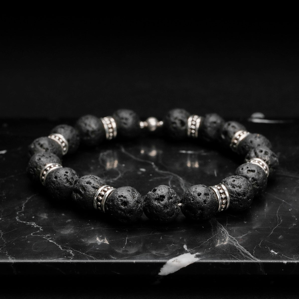 "Superset" bracelet made with volcanic stone and metallic accents, displaying a rugged and stylish design on a dark surface.