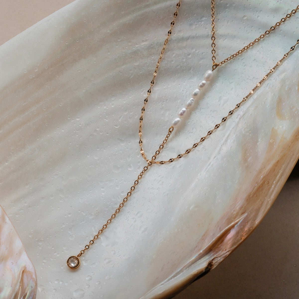 "Summersweet Necklace", a delicate necklace featuring pearls and zirconia on a gold chain, displayed on an elegant shell surface.