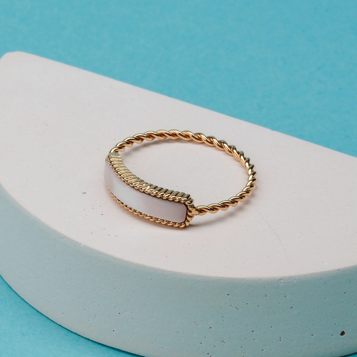 "Sumersweet Ring", une bague en or au design élégamment tordu, avec un fond bleu vif.